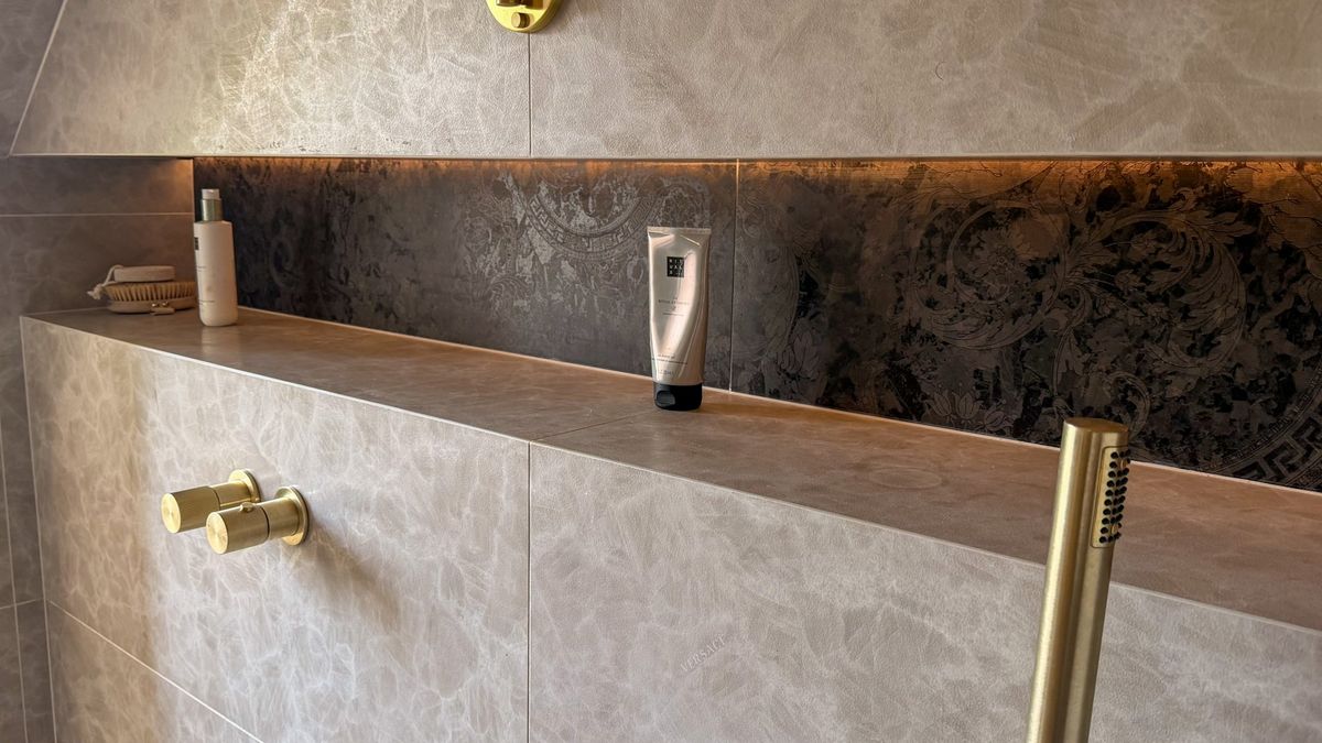 A finished Migss shower wall: large-format stone-effect tiles, an LED backlit feature niche with a mitred ledge, and brushed brass fittings.